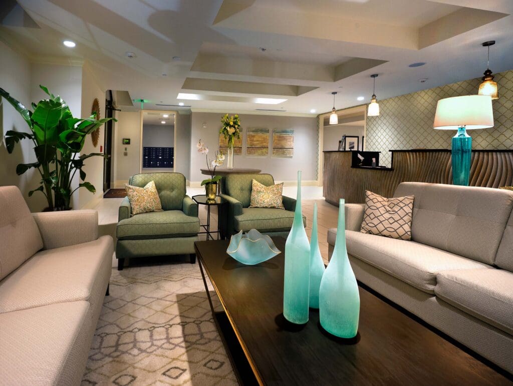 Three turquoise vases and a bowl sitting on top of a brown coffee table in the middle of two beige couches and in front of two green sofa chairs with throw pillows on them at The Magnolia at Oxford Commons near Memphis, TN.