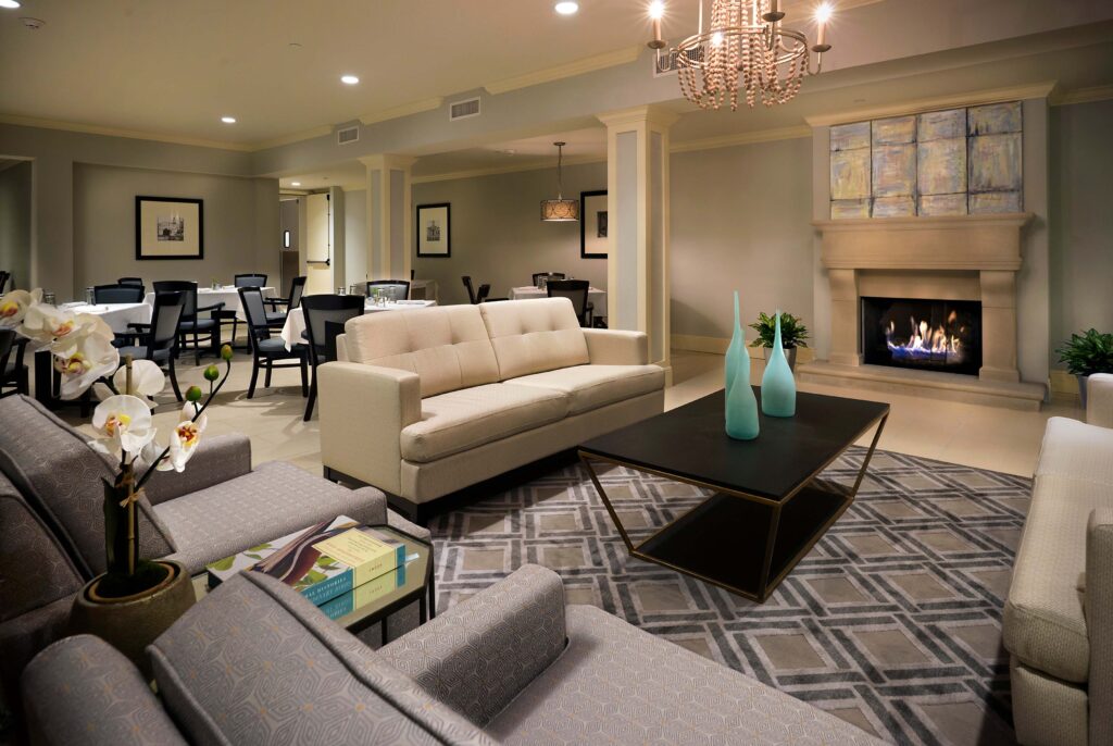A communal sitting room with a white couch, gray sofa chairs, a coffee table with three turquoise vases, and a digital fire place at The Magnolia at Oxford Commons near Memphis, TN.
