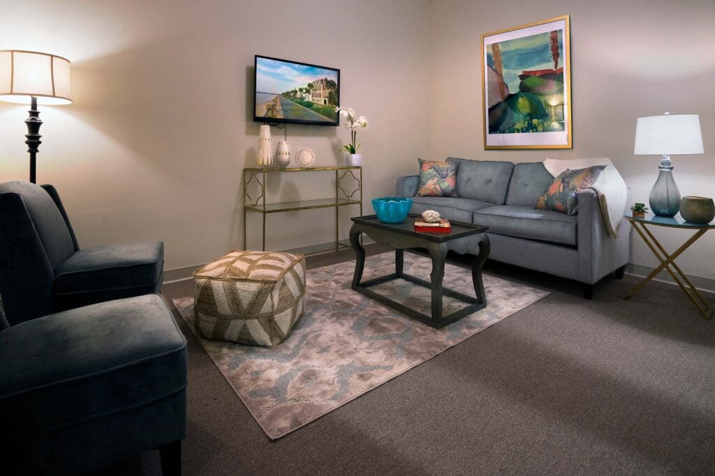 A living room with a blue couch, two sofa chairs, a coffee table, side table with a lamp, and wall art.