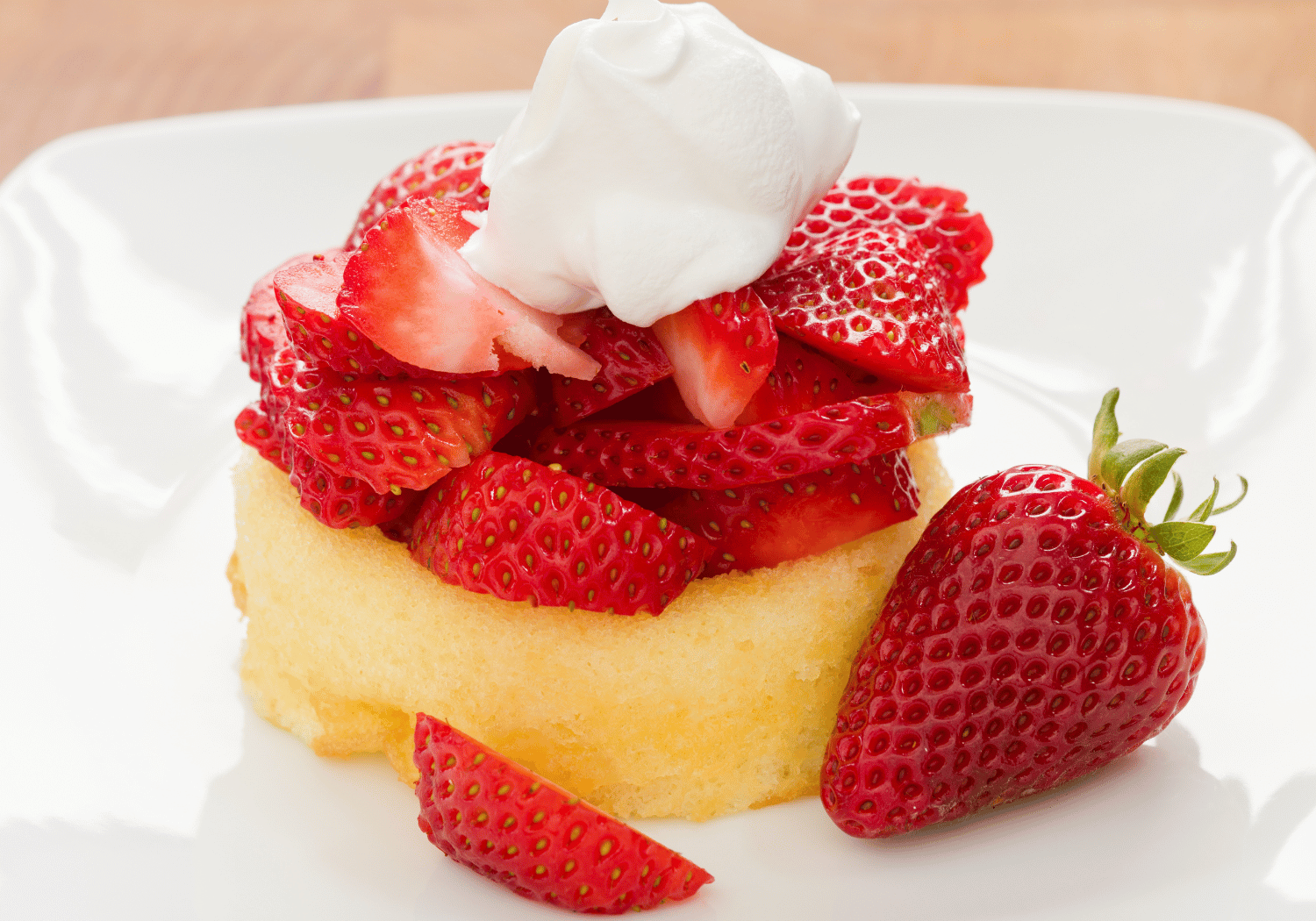 Slice of sponge cake topped with sliced strawberries and a swirl of whipped cream on a white plate.